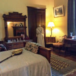 Colour photo of a room with bed, antique bed warmer, 1900s dress on mannequin
