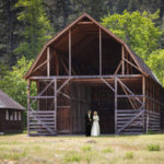 Colour photo of a man and woman walking from a large barn wearing wedding dress and suit