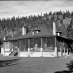 B&W photo of a heritage bungalow style manor house, hill and trees in background