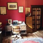Colour photo of an antique desk and chair in a room with red walls
